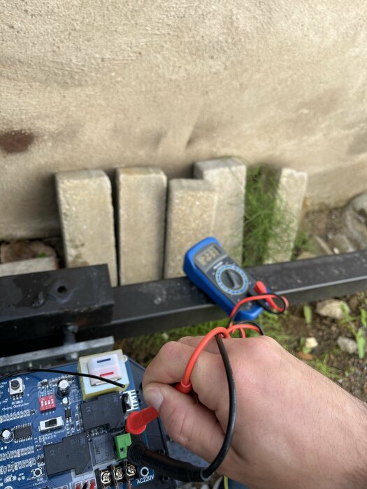 Hand mäter kretskort med multimeter. Kablar, elektronikkomponenter, suddig bakgrund, utomhus.