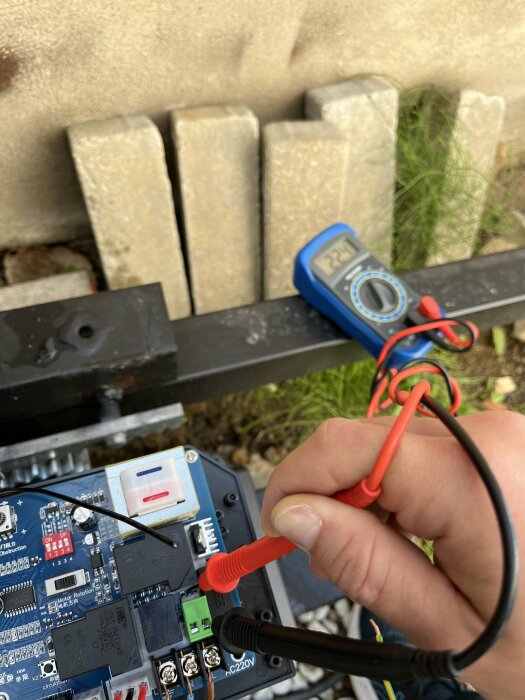 En hand med multimeterprober testar en elektrisk krets utomhus. Fokus på förgrund.