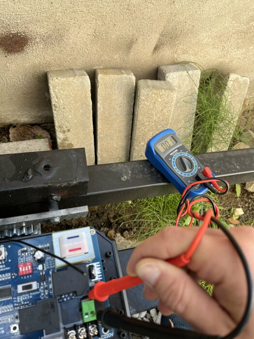 En person använder en multimeter, elektronikkomponenter och kablar på marken utomhus.