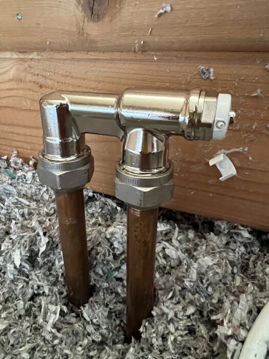 Vattenledningar och kran fastsatt på trävägg med isolering synlig vid foten.