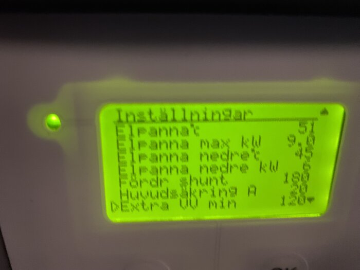 Digital display med inställningar, möjligen för en värmepanna, suddig och gröntonad bild.