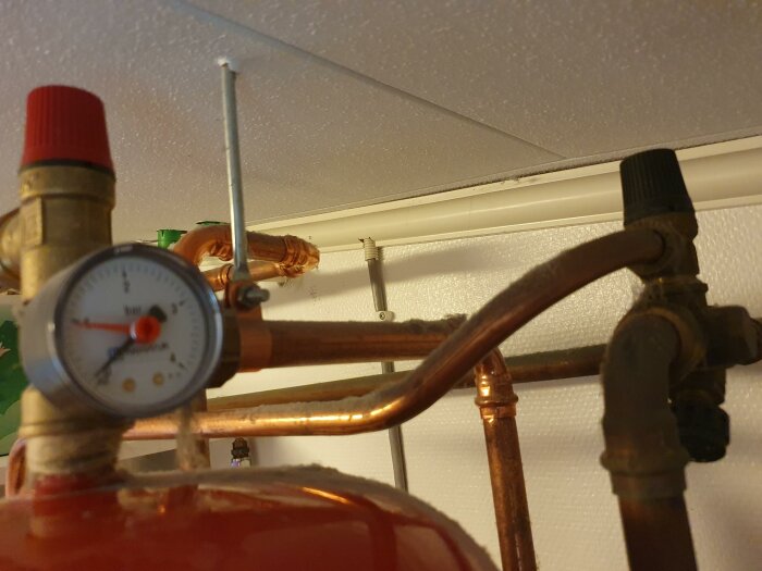 Tryckmätare på kopparledningar, ventiler, en del av röd tank, teknisk installation, oskarpt, inomhus belysning.