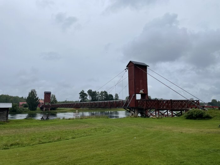 Molnig himmel, träbro med torn, flod, grönt gräs, lugn miljö, reflektion i vattnet, inga människor, landskap.