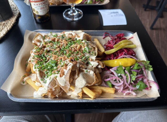 Kebabtallrik med pommes frites, sås och sallad. Öl och kvitto syns i bakgrunden.