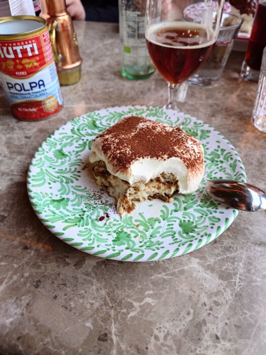 Tiramisu på ett mönstrat fat, delvis uppäten, bredvid ett ölglas och krossade tomater.