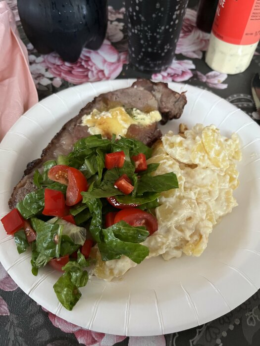 Tallrik med biff, potatissallad och spenatsallad, med dryck och såsflaska i bakgrunden.