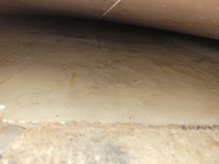 Bild under möbel visar dammigt och nedsmutsat golv med repor och skräp.