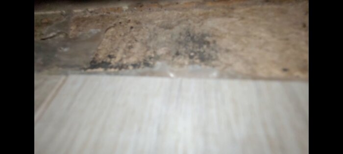 Suddig bild som visar en kant med potentiell mögel och föroreningar vid golvövergången.