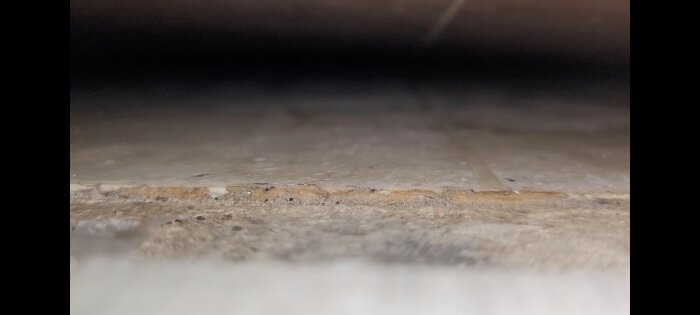 Bilden visar ett dammigt utrymme med suddig förgrund och bakgrund, möjligen under en möbel.