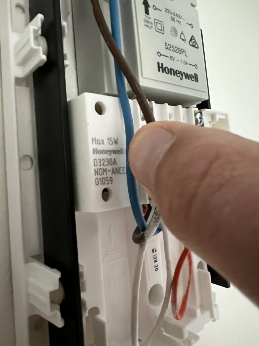 En hand manipulerar elektriska kablar vid installation av en Honeywell-enhets väggfäste.