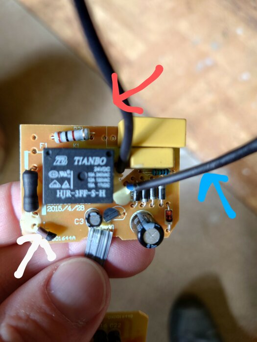 Elektronisk krets med färgmärkta pilar och hand som håller i komponent. Fokus på relä och kopplingar.