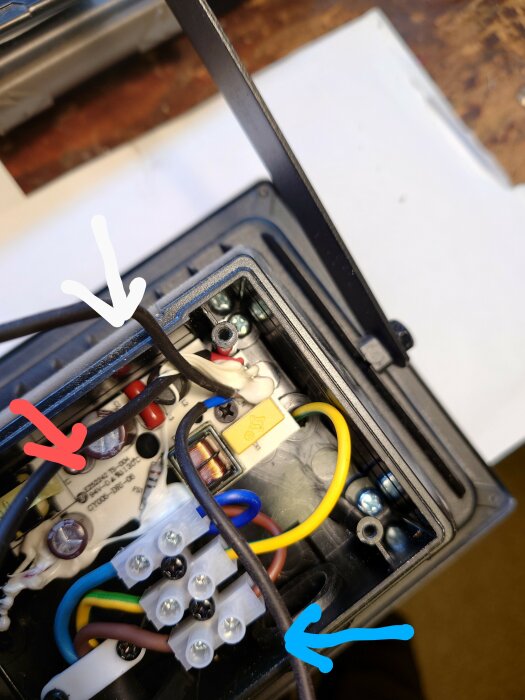 Elektrisk låda med trådar, säkring, skruvklämmor och anslutningar, öppet lock, arbetsmiljö i bakgrund.