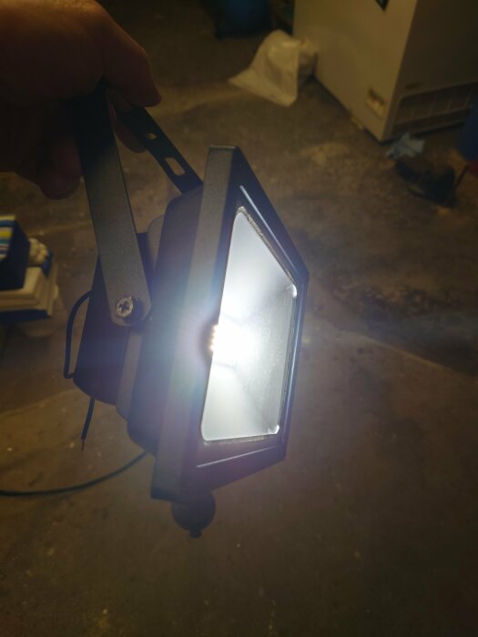 Hand håller LED-strålkastare i ett mörkt utrymme, ljuset är tänt och skiner starkt.
