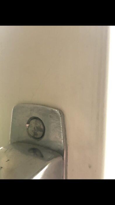 En närbild på en dörrstängare eller ett beslag monterat på en vit dörrkarm.