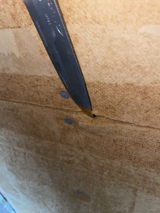 En närbild på en kniv som sticker in i en hörna av trämaterial med synliga skruvar.