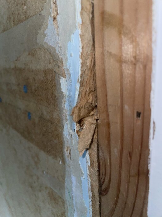 Närbild på skadad vägg och trä, med skalad färg och spackel. Tecken på renovering eller skada.