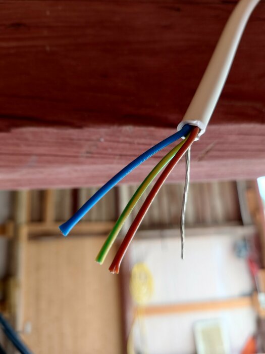 Osäkerad elektrisk kabel med exponerade koppartrådar synliga under träbjälke.