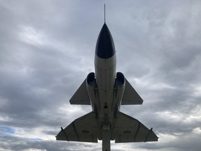 Stridsflygplan framifrån mot molnig himmel, delvis undersida synlig.