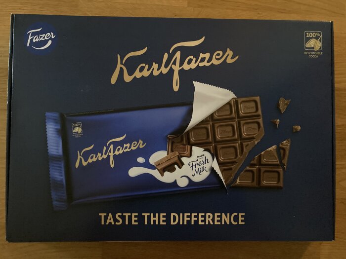 Reklampaket för Fazer Karl Fazer mjölkchoklad med brutna bitar, "TASTE THE DIFFERENCE" slogan, ansvarsfullt kakao.