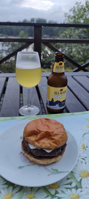 Hamburgare på tallrik och öl på bordet, med utsikt över vatten och träd.