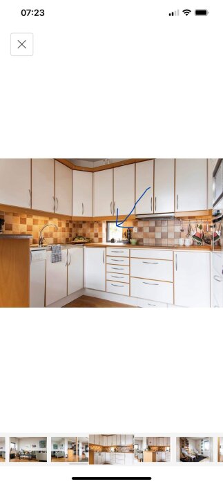 Ett kök med vita skåp, träbänkskivor, kakelvägg och en blå markering på bilden.