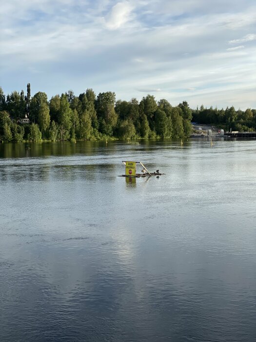 Soligt landskap med träd, flod, flytande skylt och fåglar. Lugnt vatten speglar molnformationer.