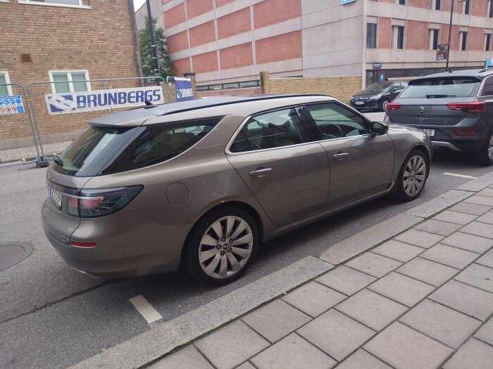 Brun bil parkerad på stadsgata, trottoarkant, andra bilar, byggnader och Brunbergs-skylt i bakgrunden.