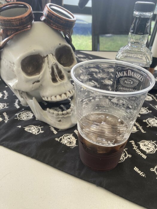 En skalle med pilotglasögon, Jack Daniels-flaska och plastmugg med mörk vätska på piratduken.