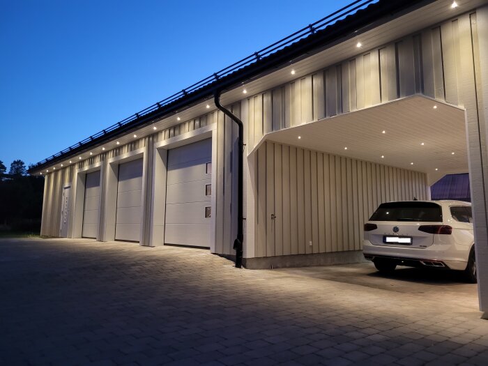 Modern garagebyggnad i skymning med flera portar och en parkerad bil under belysning.