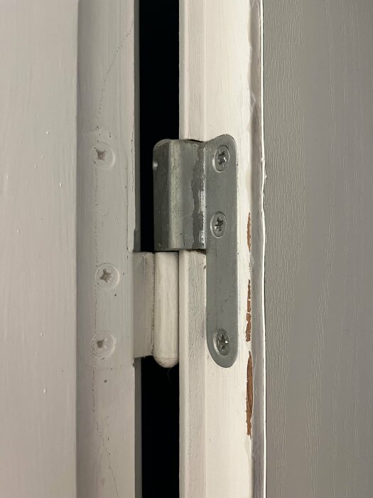Vit dörrkarm med en silverfärgad gångjärnsdel, skador på kanten, slitna målade ytor.