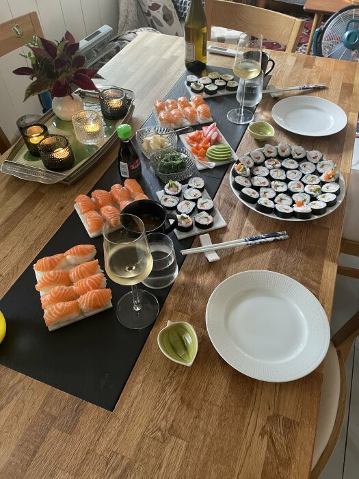 Middagsbord med sushi, wasabi, ingefära, sojasås, vin, ljus och tomma tallrikar redo för måltid.