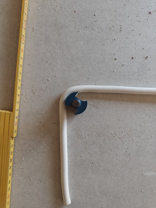 Vitmålad rörprofil med blått fäste och gult måttband på grå yta.