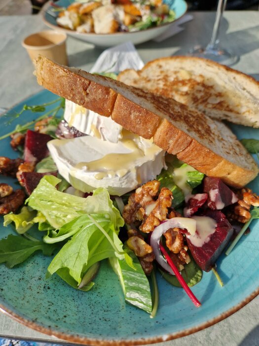 En tallrik med sallad, rostbröd och en stor bit Brieost, färsk sallad, rödbetor och valnötter i solljus.