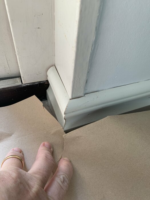 En hand pekar på en möjlig golvskada nära en vit dörrkarm.