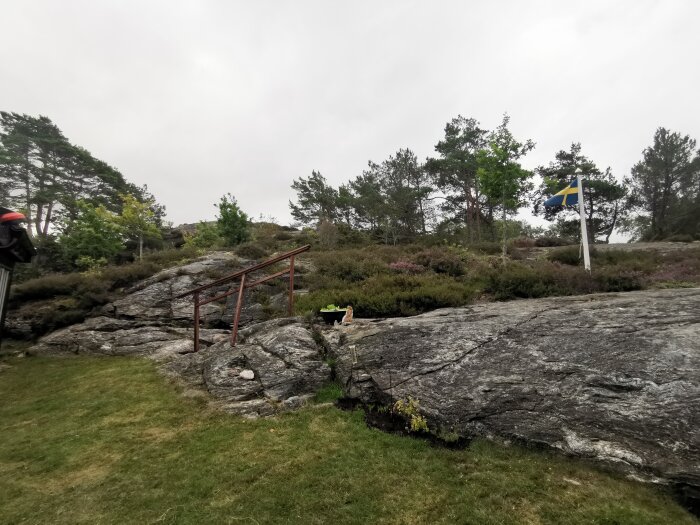 Natur, klippor, svensk flagga, räcke, grön vegetation, dimmig himmel, utomhus, dagtid.