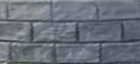 Suddig bild på mönstrad yta, liknar gråa tegelstenar eller murverk. Detaljer ej tydliga på grund av bildens kvalitet.
