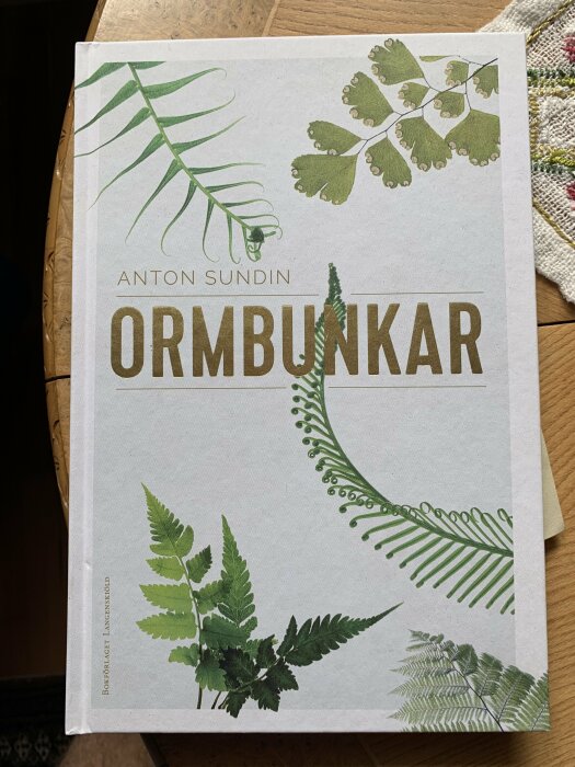 Bokomslag med växter; titeln "ORMBUNKAR" av Anton Sundin; gröna ormbunkeblad på ljus bakgrund.