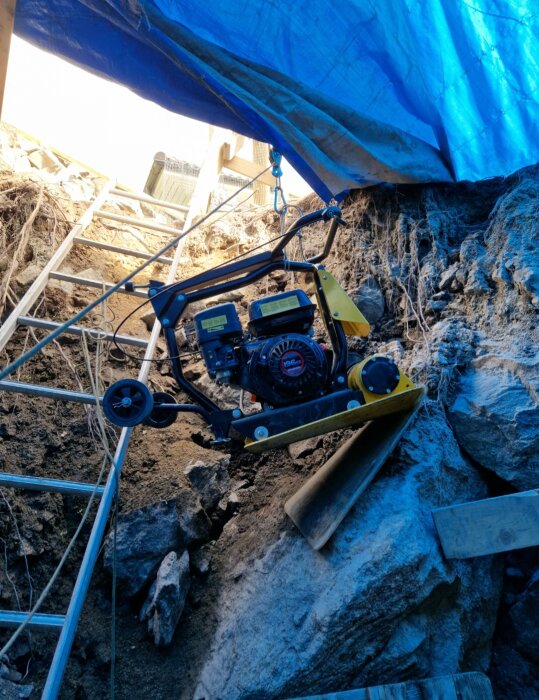 Byggarbetsplats, blå presenning, generator, stegar, klippor och jord. Utomhus, konstruktion eller renoveringsprojekt, teknisk utrustning.