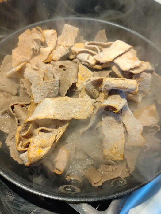 Tunnbröd värms i en stekpanna, ånga, kokande vatten undertill, matförberedelse, köksmiljö.