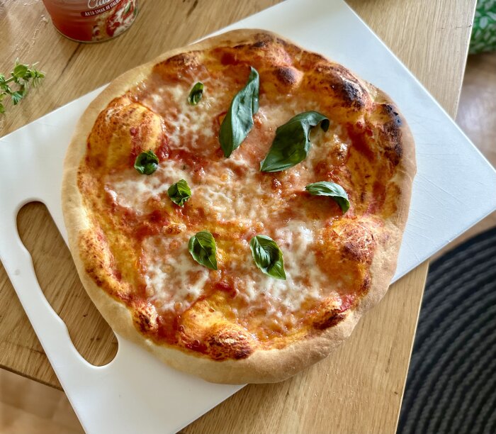 Nybakad pizza med tomatsås, ost och basilikablad på skärbräda, hemmiljö.