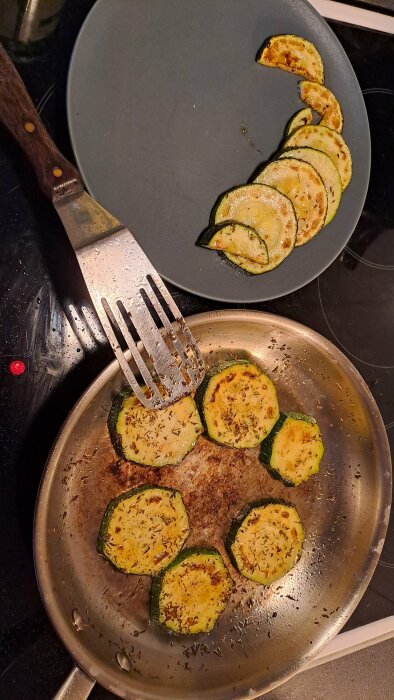Stekt zucchini i stekpanna med kryddor, tillsammans med spade och keramiktallrik.