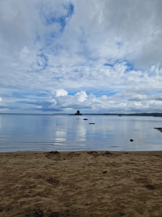 Strand, lugnt vatten, molnig himmel, avlägsen ö, sand, reflektioner i vatten, natur, dagtid.