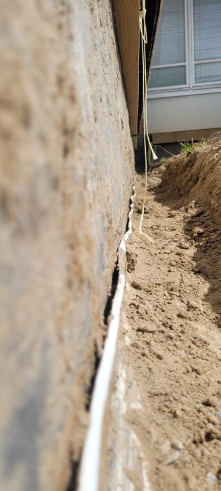 Grund till hus med kabel längs spricka och sandig mark, oskarp bakgrund med fönster.