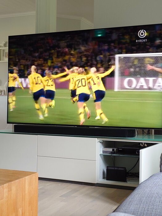 Firande fotbollsspelare på TV-skärm i vardagsrum, sannolikt målglädje, direktsändning på svensk kanal.