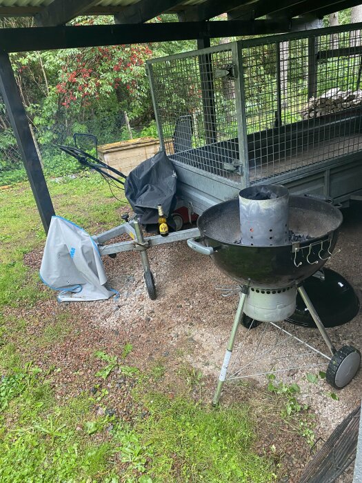 Trädgård med grill, cykel och kaninbur under ett takskydd, vardaglig och oordnad exteriör.