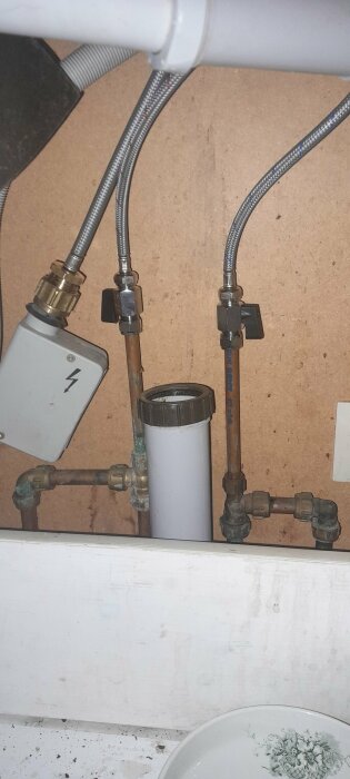VVS-installation under handfat med ledningar, rörkopplingar och vattenfilter.