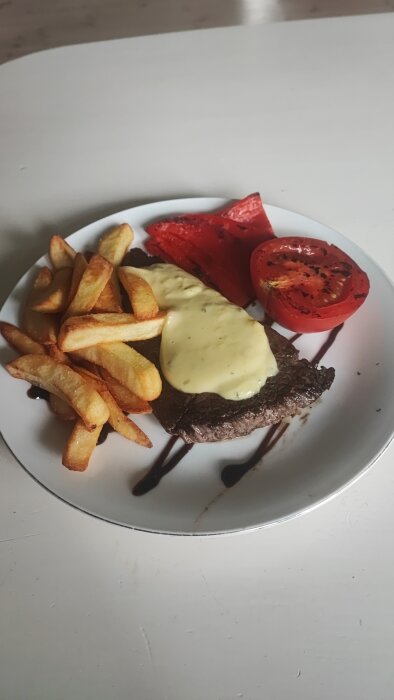 Stekt biff med bearnaisesås, pommes frites och grillad tomat på vit tallrik.