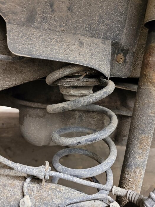 Fjäder i bilens hjulupphängning, smutsig, möjligen en skruv fjädersättning, närbild, slitage, täckt i damm.