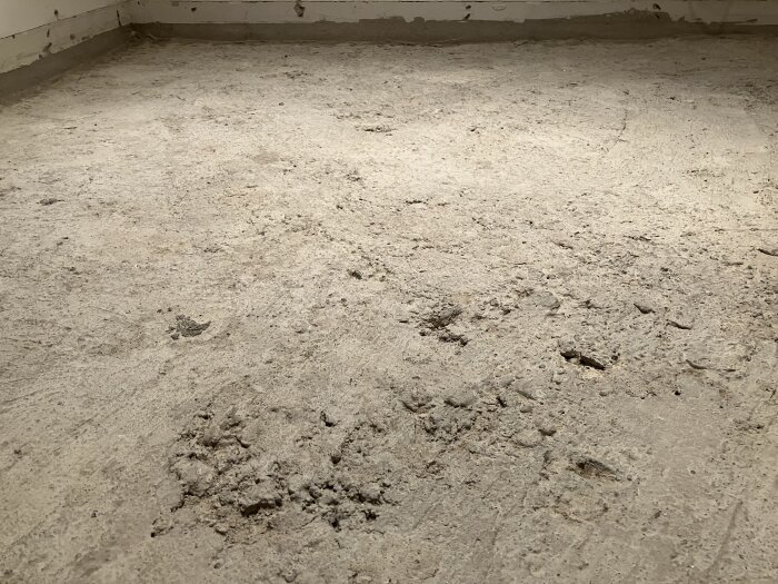Ojämn betonggolv inne i ett rum, dammigt och smutsigt, med spår av konstruktion eller renovering.