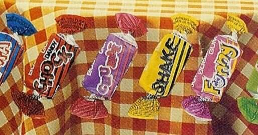 Olika godisbitar på rutig bakgrund. Färgglada inslagningar. Choklad. Snacks. Sötsaker. Festligt.